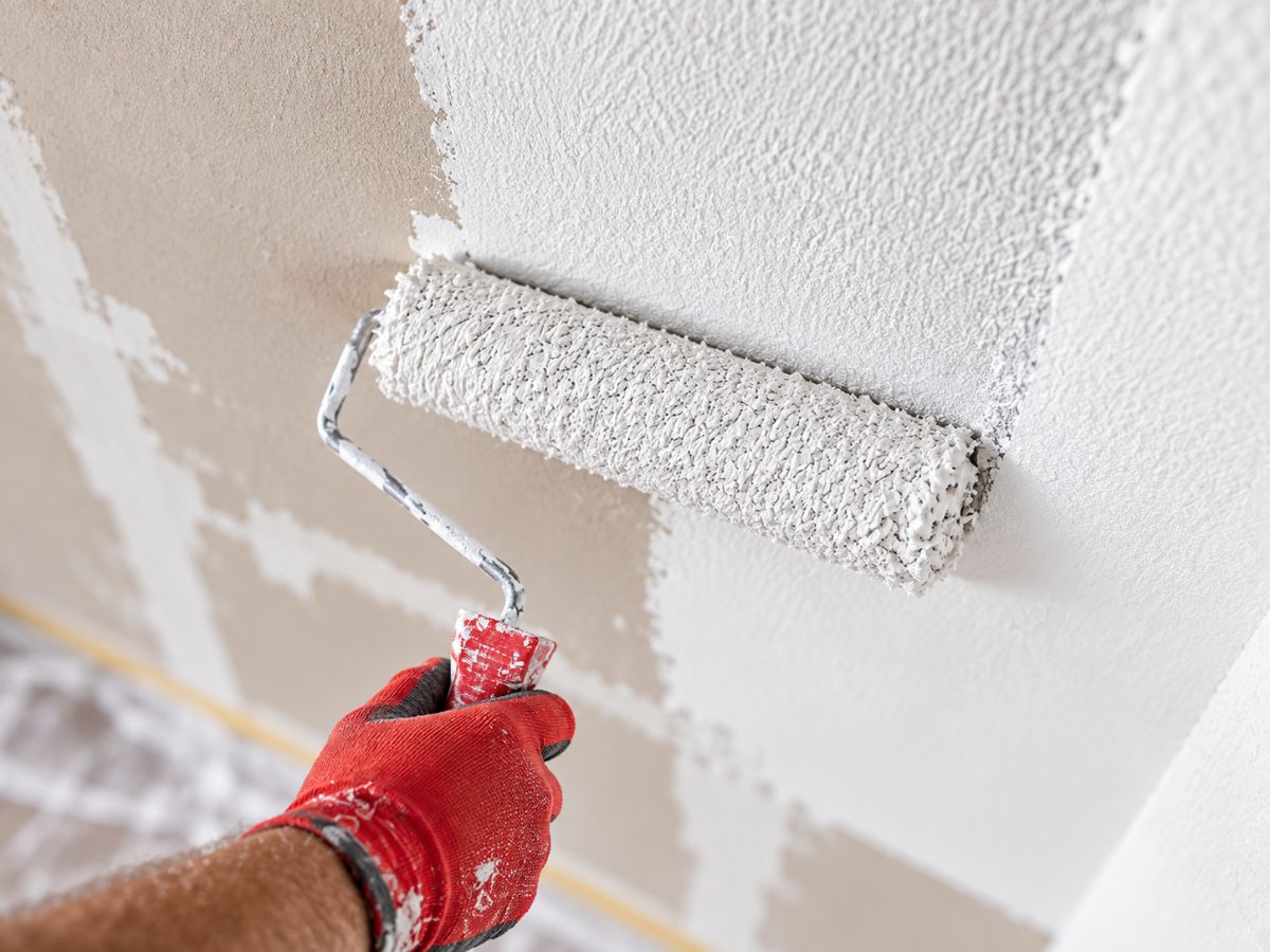 Farbrolle trägt weiße Wandfarbe auf eine Innenwand auf
