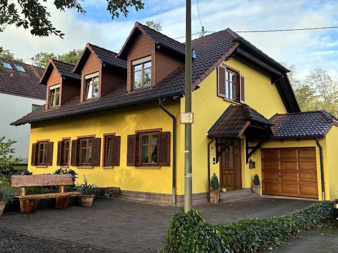 Fassadenanstrich in Gelb mit braunen Fensterläden und Holzgauben