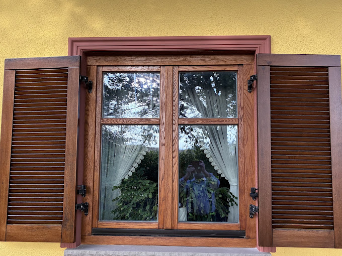 Holzfenster mit frisch lackierten Fensterläden vor gelber Fassade