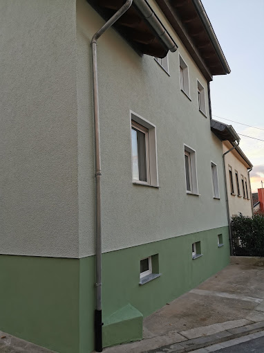 Hausecke mit hellgrauer Fassade und grünem Sockel