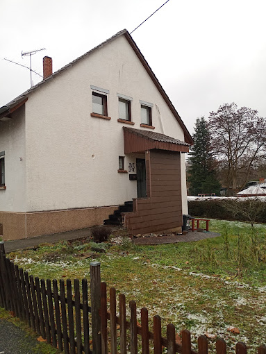 Weißes Wohnhaus mit braunem Sockel und Außentreppe